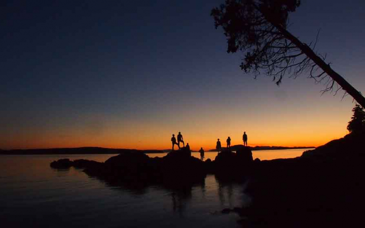 the silhouette of six people standing on rocks in the water at sunset